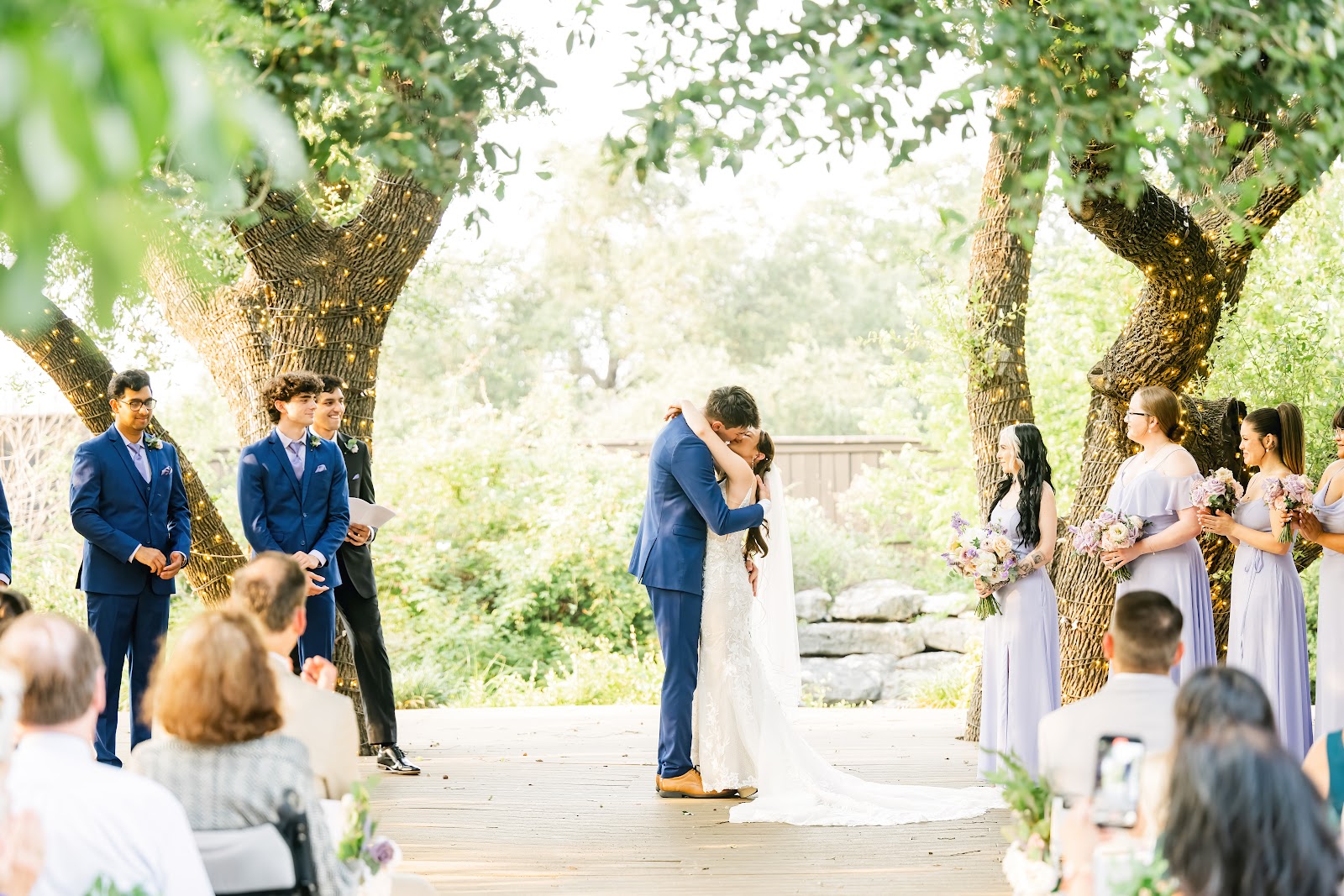 A couple kissing at the end of a ceremony on the wooden platform under the oaks