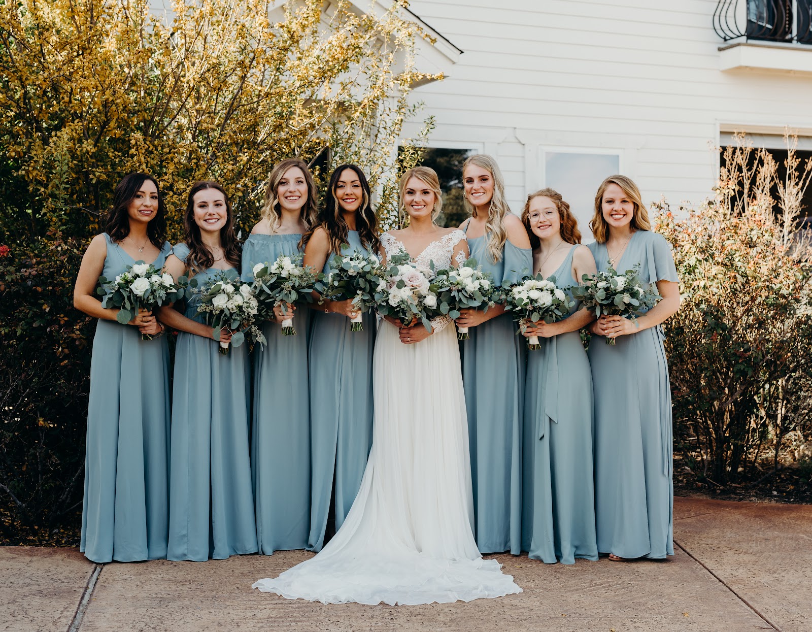 A bride with her bridesmaids in sage dresses in front of the white house